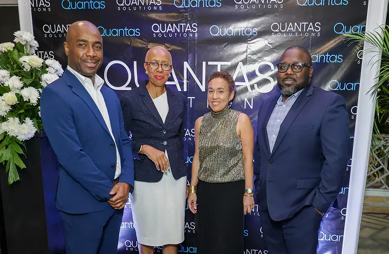 Business professionals at Quantas Solutions event, diverse team of corporate executives in formal attire, standing in front of Quantas Solutions branded backdrop, showcasing leadership in finance and investment services.