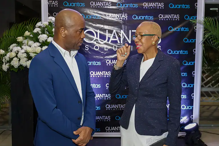 Professional woman and man engaged in conversation at Quantas Solutions event, standing in front of a branded backdrop, dressed in business attire, representing financial and investment solutions.
